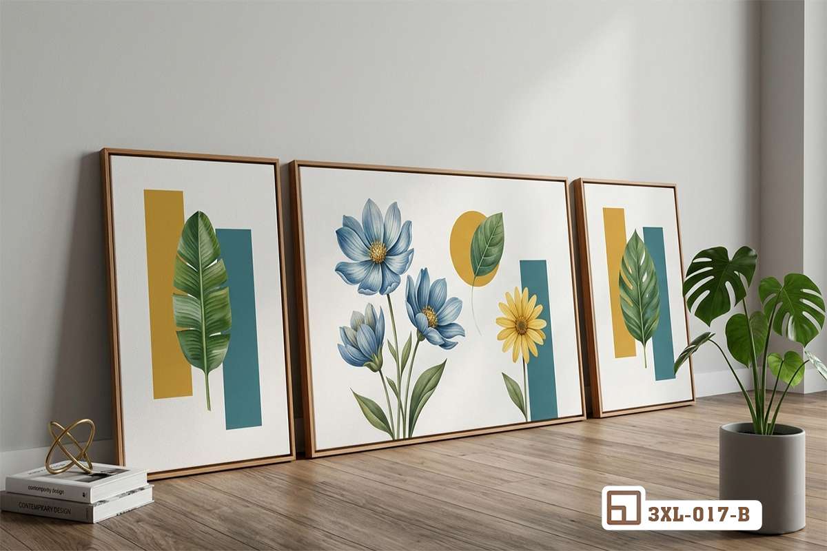 Bộ tranh hoa lá nghệ thuật đặt dựa tường sàn gỗ tự nhiên bên chậu cây xanh Ba bức tranh hoa lá tối giản tone xanh vàng đặt trên nền sàn gỗ kế chậu cây